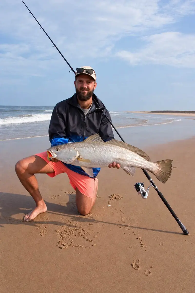Angler kneeling on the sand with a kob in warm light under a blue sky