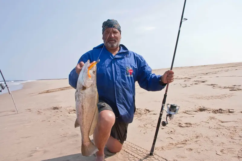 Angler kneeling on the beach with a kob and his rod